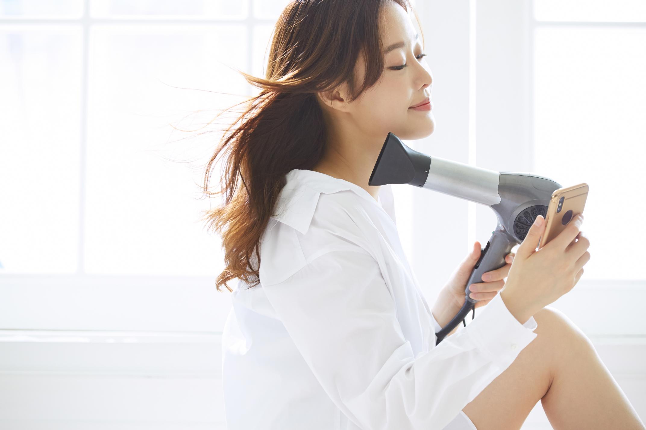 長髮女子用吹風機吹乾頭髮